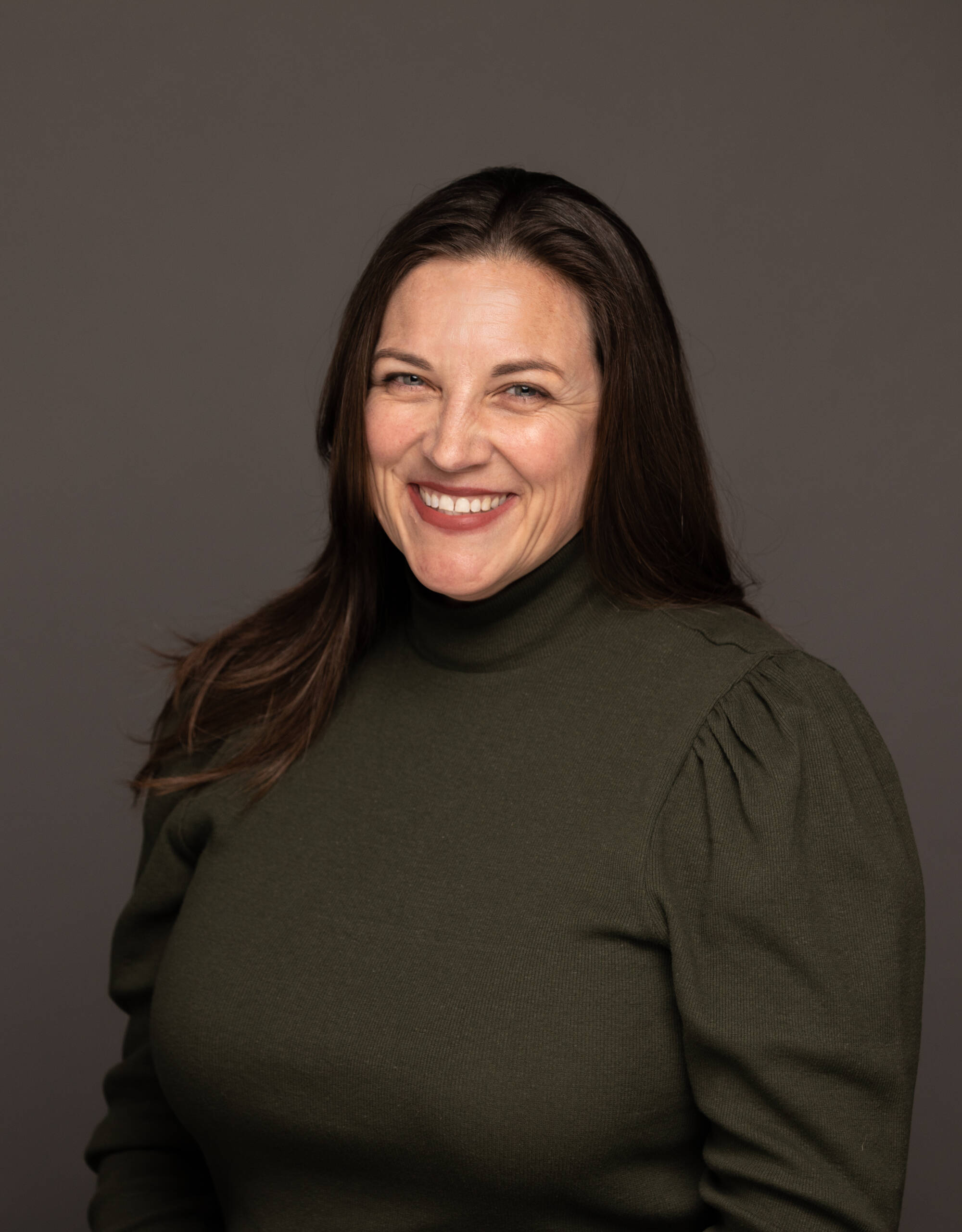 Alison Hodgson in a green long sleeve turtleneck on a dark background with red lips.